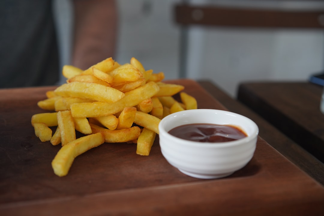 A pile of chips on a wooden board, with a small bowl of gravy beside them