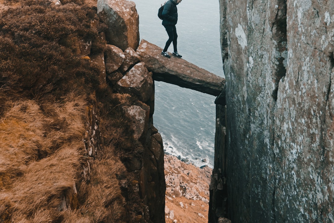 A walker crossing a narrow rock ledge spanning a gap in a sea cliff