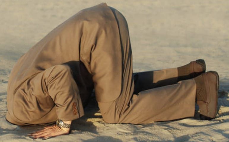 A man in a suit with his head buried in the sand